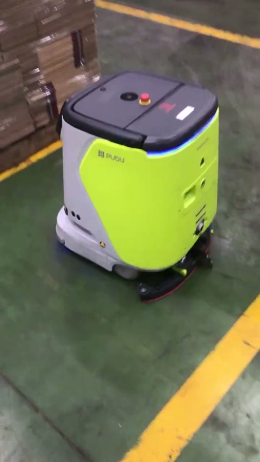 Robot CC1 màu xanh chanh đang chà sàn cạnh pallet thùng carton